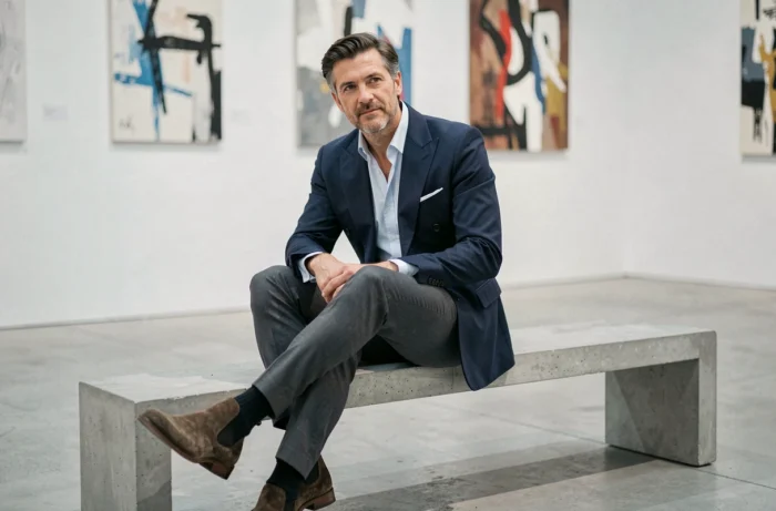 Homme en blazer marine double boutonnage assis dans une galerie d'art contemporaine, style élégant et raffiné tendance mode masculine